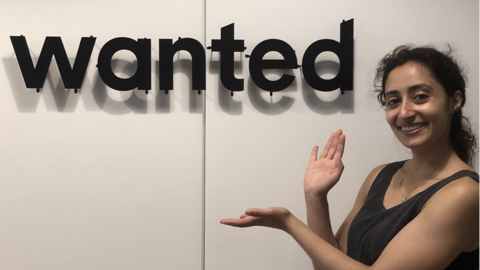 Salma Siddiqui posing next to a sign displaying the "wanted" logo. 