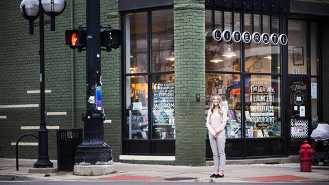 SI 311 student Samantha Greenhill stands and smiles at a corner intersection outside Literati Bookstore in downtown Ann Arbor. 