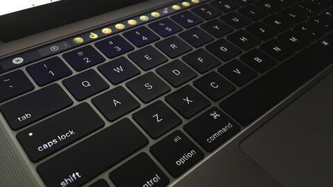 Laptop keyboard with a line of emoji choices on the touch bar.