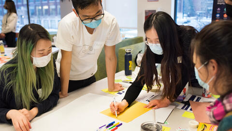 Four students standing around a table and writing with markers