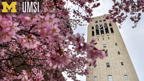 A Zoom background showing Burton Memorial Tower framed by tree branches covered in pink blossoms. A Block M logo with letters UMSI is overlaid in upper lefthand corner.