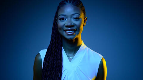 Shelby in black and blue light smiling at the camera and wearing a white shirt. 