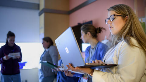 MHI student Emily Trumpower wearing a white lab coat and looking at a laptop. 