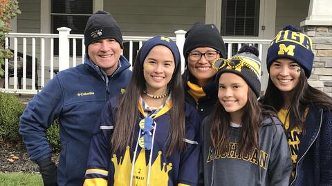 Mike and Lisa Burke with their three daughters dressed in University of Michigan apparel, standing outside. 