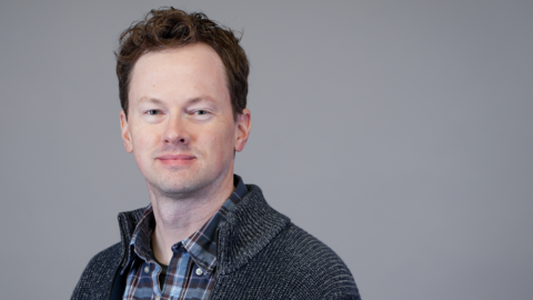 A professional headshot of Jeremy Barney wearing a gray cardigan. 