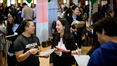 Students gathering at a UMSI career fair. One student smiles and talks with an Amazon employee. 