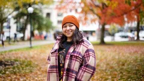 UMSI BSI student Zochil Moreno-Martinez standing outside during fall, wearing a hat and smiling. 