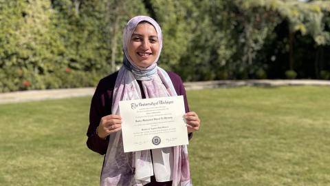 University of Michigan Master of Applied Data Science degree program graduate Rania El-Shenety smiles and poses outdoors while holding her University of Michigan master’s diploma in applied data science. 