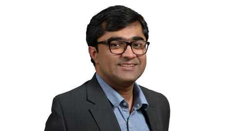 Mustafa Naseem wearing a suit and glasses and smiling at the camera. 