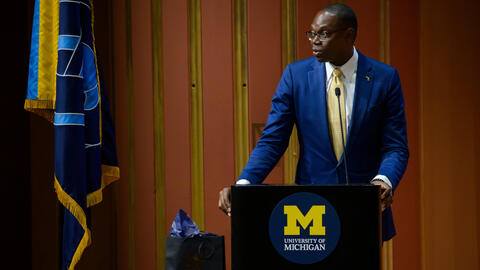 Lt. Gov. Garlin Gilchrist II stands at a podium adorned with the University of Michigan logo