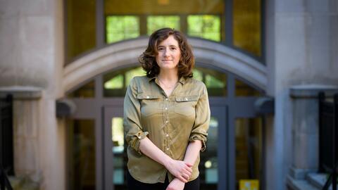 Assistant professor Abigail Jacobs stands in front of an academic building on the University of Michigan campus. 