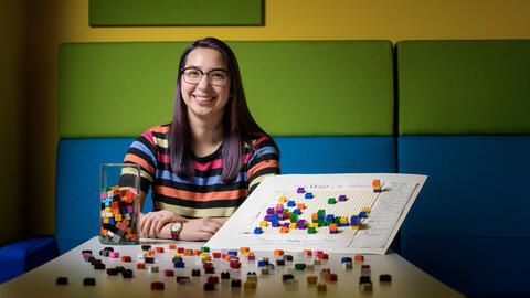 Elsie sitting at a table with lego bricks strewn across the surface and sitting next to a Lego block graph data visualization.