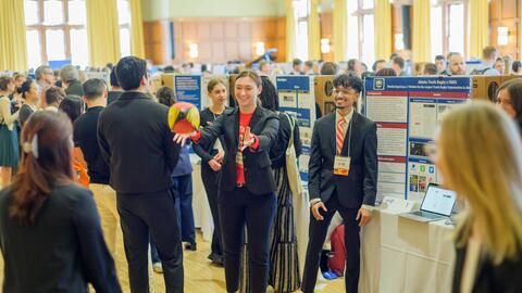 Students standing in front of a trifold display in the ballroom of the Michigan League toss around a rugby ball 