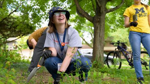 A UMSI student holds a shovel and smiles while working in a rain garden 