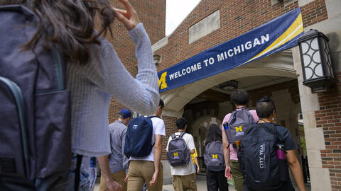 A photo of students wearing UMSI backpacks walking toward an arch with a University of Michigan banner clearly displayed at the entrance