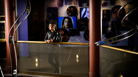Tam Rayan wears a leather jacket and short hair and leans on a railing at the Arab American National Museum. 