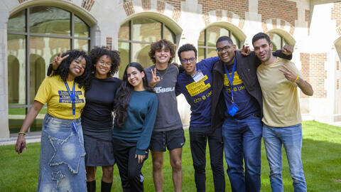 Seven CCSI fellows pose on the grass outside of North Quad, smiling and holding up peace signs