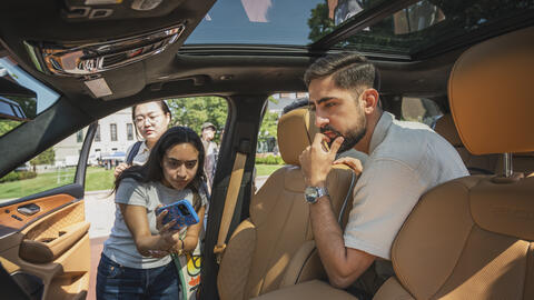An interior view of a vehicle as three UMSI students study the user interface, with one taking a photo on their cell phone