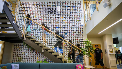 A side view of an open, modern staircase with high school students climbing up it, wearing backpacks