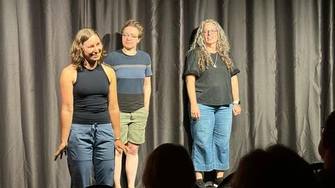 Gabriela Marcu gestures on stage with two other people beside her