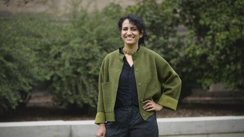 Amina Abdu smiles into the camera while standing outside wearing a green cardigan. 