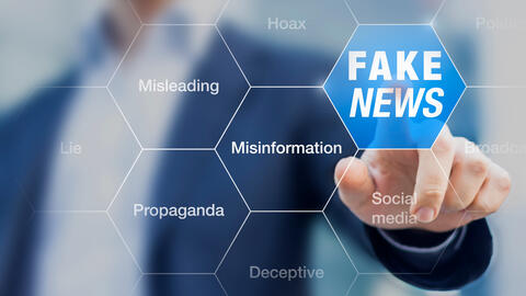 A photo of a man in a suit clicking on a clear screen with a variety of bubbles that read misleading, propaganda, deception and fake news.