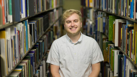 Austin Book poses in the library stacks with books on either side of him