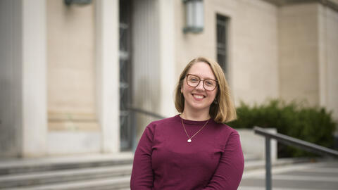 Rebecca Frank wearing a maroon sweater, a neckplace and glasses and smiling at the camera. 