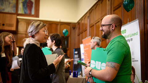 A student chats with a recruiter wearing a green shirt and holding a folder with the Duo logo