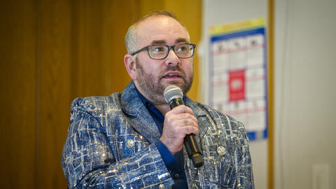 Oliver Haimson wearing a blue blazer and glasses and holding a microphone at his book launch. 