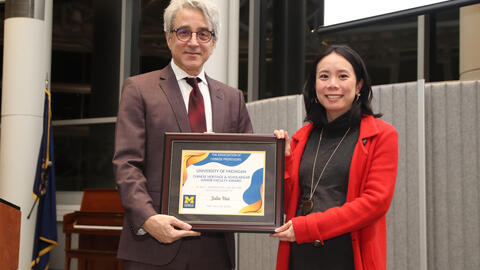 Arthur Lupia and Julie Hui stand next to each other holding Julie's award and smiling into the camera. 