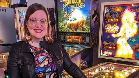 Jackie DiOrio standing next to a row of brightly lit pinball machines.