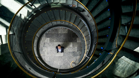 Overhead view of Kentaro Toyama standing at the center of a circular spiral staircase, looking up. 