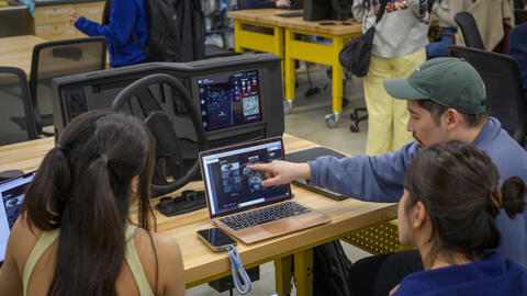 Three people face a computer screen and car dashboard prototype, as one collaboratively points to an element on-screen