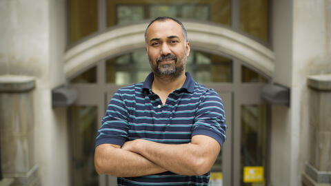 Joyojeet Pal stands outside cross armed in a striped blue shirt. 