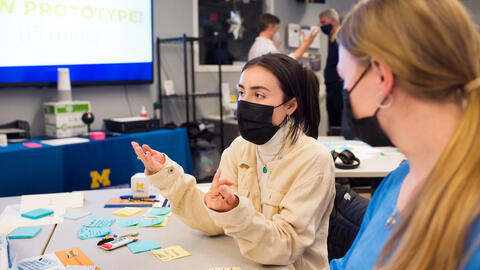 Two students discussing at a table covered in sticky notes and markers