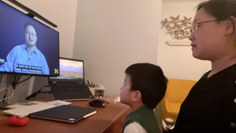 Yao Wei sits at a desk with her son on her lap and watches a lecture by UMSI professor Qiaozhu Mei.
