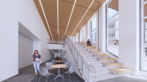 A modern stairwell leads to a second floor in a large atrium. The side of the stairwell has platform seating integrated among the steps. People walk through the hall.