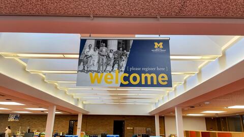 A sign that reads "Welcome [please register here]", with the Bentley historical logo, hangs from the ceiling