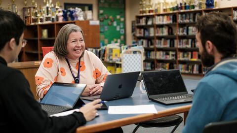 Katie Burrill smiles, seated at table with Garret Potter and Liyang Qu. Each has a laptop in front of them.