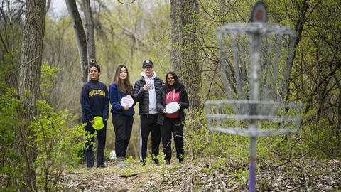 Four people stand in the woods at a disc golf course