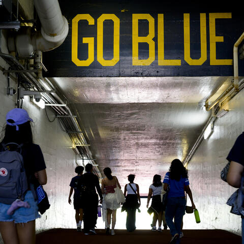 Students walk under a "Go Blue" mural in the tunnel entering the field at Michigan Stadium
