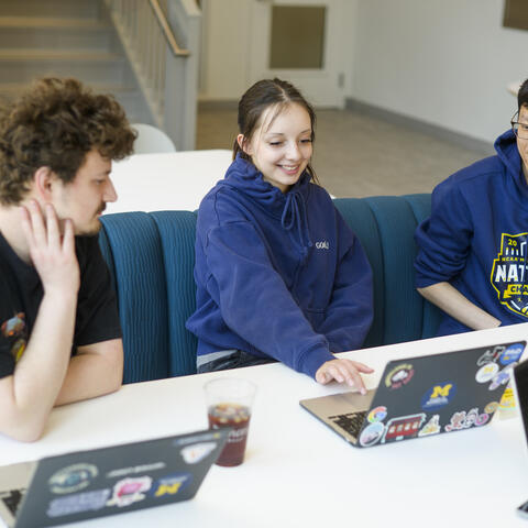 PhD students sitting and talk and look over computer screens.
