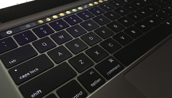 Laptop keyboard with a line of emoji choices on the touch bar.