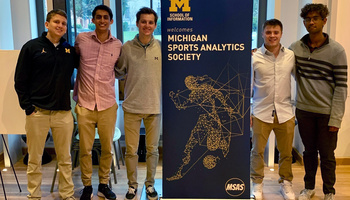 The Michigan Sports Analytics Society leadership board poses with a banner that reads “School of Information welcomes Michigan Sports Analytics Society” at the Michigan Sports Analytics Symposium, March 30, 2022 in North Quad Space 2435. 