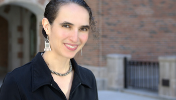 Professor Tanya Rosenblat smiles at the camera. She is standing in front of a brick building on the University of Michigan campus. 