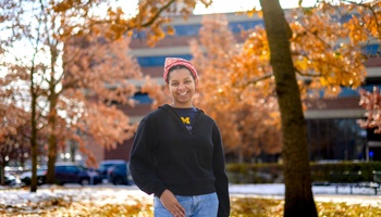 An image of Christine Carethers standing on the U-M campus surrounded by fall foliage.
