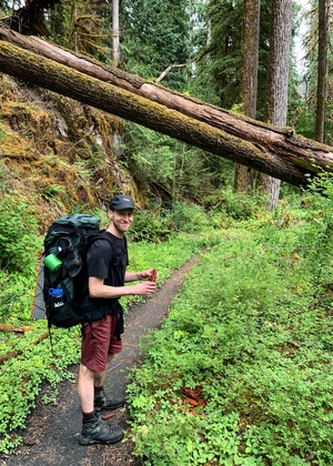 Dallas Card wears a backpack while pausing on a hiking trail in Olympic National Park.