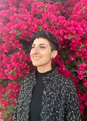 A headshot of Tam Rayan standing in front of a bush full of flowers