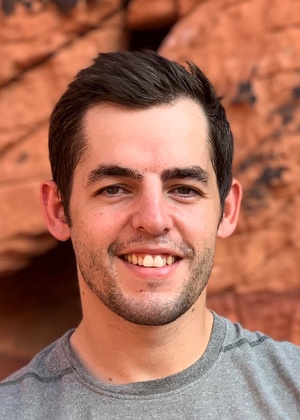 A headshot of Luke Anger in front of a wall of red rocks.
